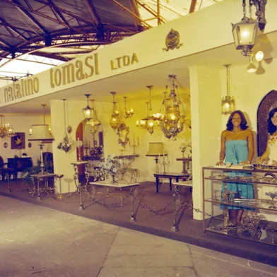 Febre nas residências dos anos 1960, 1970 e 1980, as peças produzidas pela Metalúrgica Natalino Tomasi até hoje são facilmente identificadas, assim como as da Eberle e as do lendário Artesanato Nigavel. Lustres, lampiões, candelabros, luminárias, mesas de cabeceira, cadeiras, castiçais, incensários, fruteiras, abajures, espelhos, arandelas, apliques, porta-retratos, porta-bíblias e uma infinidade de artefatos em metal podiam ser encontrados em diversas lojas de Caxias e região.A apurada técnica do “artesanato em bronze retocado a mão” de Natalino Tomasi também costumava ser exposta na Festa da Uva. Legenda: estande da Metalúrgica Natalino Tomasi na Festa da Uva de 1978, junto aos Pavilhões.<!-- NICAID(16224986) -->