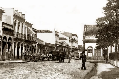 Irmãos Ferrari / Acervo Ronaldo Bastos Rua 15 de Novembro, a atual Rua José Montaury, por volta de 1900.Aparece o Salão Grau, restaurante onde foi fundado o Grêmio em 1903. Praça XV ainda com cercamento.<!-- NICAID(16365130) -->