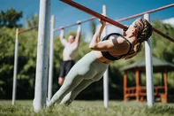 Two individuals perform calisthenics exercises in an urban park, utilizing outdoor bars on a sunny day, promoting fitness and a healthy lifestyle.<!-- NICAID(16237938) -->