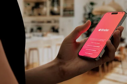 Hand holding a smartphone with Tinder app open, ready to swipe in a cozy home settingFonte: 833820534<!-- NICAID(15906850) -->