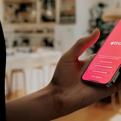 Hand holding a smartphone with Tinder app open, ready to swipe in a cozy home settingFonte: 833820534<!-- NICAID(15906850) -->