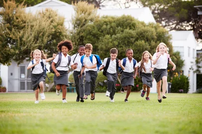 Excited Elementary School Pupils Wearing Uniform Running Across Field At Break Time<!-- NICAID(15805972) -->