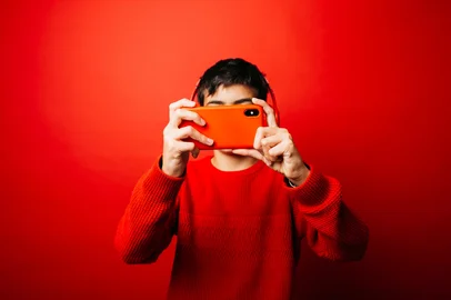 Pre-adolescent boy wearing a red sweater and red headphones over a red background, taking a selfie with a red smartphoneIndexador: Jordi SalasFonte: 553437456<!-- NICAID(16101438) -->