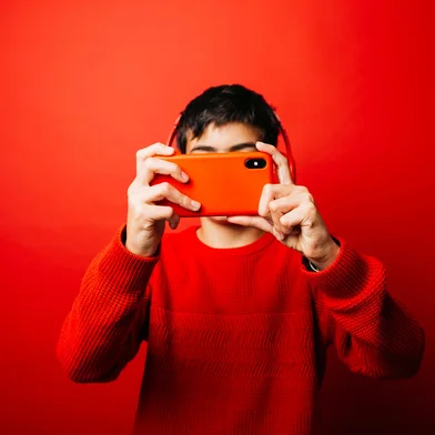 Pre-adolescent boy wearing a red sweater and red headphones over a red background, taking a selfie with a red smartphoneIndexador: Jordi SalasFonte: 553437456<!-- NICAID(16101438) -->