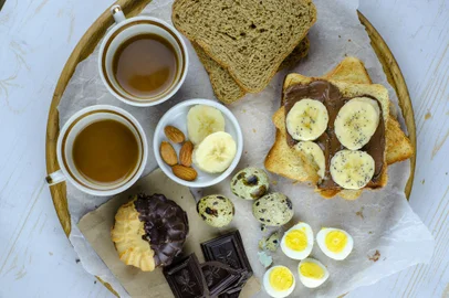 Large selection of breakfast food on a table with quail eggs, cookies,  toasts, chocolate, banana, yogurt, chocolate butter, nuts served with coffee viewed from above - Foto: Zkolra/stock.adobe.comFonte: 270773208<!-- NICAID(15288303) -->