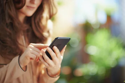 Green Home. Closeup on middle aged woman at home in sunny day using smartphone applications.<!-- NICAID(15769189) -->