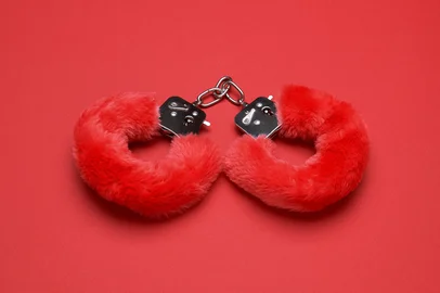 Red sexy fluffy handcuffs on a red background<!-- NICAID(16072411) -->