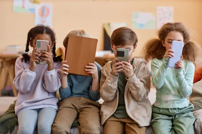 Seventyfour / stock.adobe.com Group of young children holding smartphones and hiding faces, gen Alpha, Crianças no celular <!-- NICAID(15977799) -->