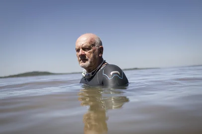 PORTO ALEGRE, RS, BRASIL, 09-10-2025: O nadador master Fracismar Siviero, 70 anos, à beira do Lago Guaíba, no bairro Belém Novo, onde costuma treinar para travessias em águas abertas. Em 2023, ele precisou passar por uma cirurgia cardíaca e recebeu seis pontes de safena. Pouco tempo depois do procedimento, o atleta voltou aos treinos e, entre 2024 e 2025, já soma doze participações em maratonas aquáticas no Brasil e no exterior. Foto: Mateus Bruxel/Agência RBSLocal: Porto AlegreIndexador: MATEUS BRUXEL<!-- NICAID(16182698) -->