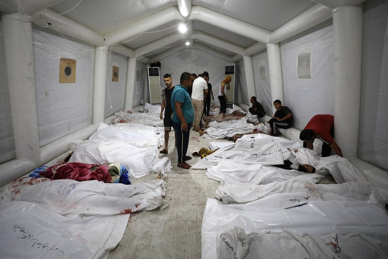 EDITORS NOTE: Graphic content / People stand over bodies of Palestinians killed after a blast ripped through the Ahli Arab hospital in central Gaza after they were transported to Al-Shifa hospital, on October 17, 2023. Israel and Palestinians traded blame for the incident, which an "outraged and deeply saddened" US President Joe Biden denounced while en route to the Middle East. (Photo by Dawood NEMER / AFP)<!-- NICAID(15571867) -->