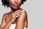 Beauty routine. Close up of young African woman applying body cream and smiling while standing against grey backgroundIndexador:                                 Fonte: 237545816<!-- NICAID(14646768) -->