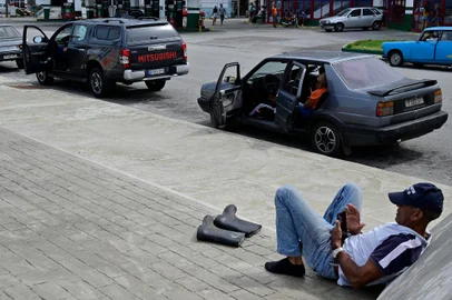 Um homem olha para o seu telemóvel ao lado de motoristas que esperam para abastecer os seus carros num posto de gasolina em Havana, em 18 de outubro de 2024, durante um apagão nacional causado por uma falha na rede. As avarias técnicas, a escassez de combustível e a elevada procura têm feito com que as centrais termoeléctricas do país falhem constantemente, obrigando o governo a declarar emergência energética e a tomar medidas como o encerramento de escolas e fábricas.<!-- NICAID(15893973) -->