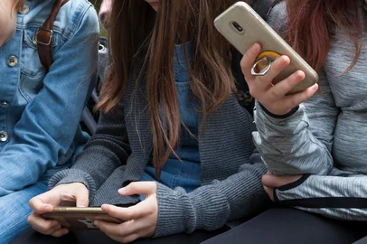 Two young teenage girls sitting holding smartphones in their hands. Teens, kids playing around, checking their phones Phone addiction or young preteens using modern technology in everyday life conceptFonte: 291107222<!-- NICAID(16101437) -->