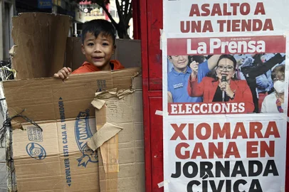 A boy plays next to a newsstand with a poster showing left-wing opposition candidate Xiomara Castro, in Tegucigalpa on November 29, 2021, a day after general elections in Honduras. - Left-wing opposition candidate Xiomara Castro took a commanding lead over the ruling party's Nasry Asfura, preliminary results showed. With just over half of votes counted, former first lady Castro had taken more than 53.5 percent with Asfura a distant second out of 13 candidates with 34 percent, according to a National Electoral Council (CNE) live count. (Photo by Orlando SIERRA / AFP)<!-- NICAID(14958229) -->