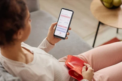 Seventyfour / stock.adobe.com Girl Holding Phone with Period Tracker AppHigh angle closeup of young woman holding smartphone with period tracker app on screen and holding hot water bottle on belly copy space. Foto: Seventyfour/ stock.adobe.comFonte: 787073360<!-- NICAID(16382958) -->