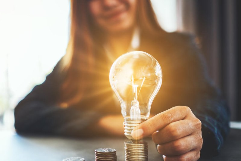 Businesswoman holding and putting lightbulb on coins stack on table for saving energy and money conceptFonte: 314277037<!-- NICAID(14411069) -->