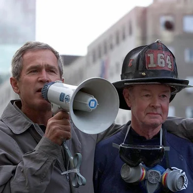 (FILES) US President George W. Bush (L), standing next to retired firefighter Bob Beckwith, 69, speaks to volunteers and firemen as he surveys the damage at the site of the World Trade Center in this 14 September 2001 file photo in New York. The New York City Fire Department announced on February 5, 2024, the death of retired firefighter Robert Beckwith, who rushed to the scene of the September 11, 2001 attacks and became famous for standing next to President George W. Bush on the ruins of the World Trade Center. (Photo by Paul J. RICHARDS / AFP)<!-- NICAID(15670914) -->