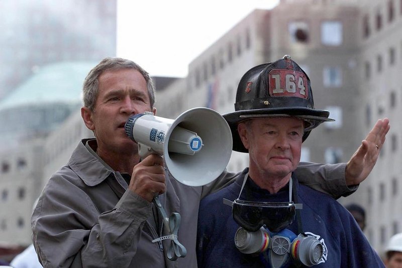(FILES) US President George W. Bush (L), standing next to retired firefighter Bob Beckwith, 69, speaks to volunteers and firemen as he surveys the damage at the site of the World Trade Center in this 14 September 2001 file photo in New York. The New York City Fire Department announced on February 5, 2024, the death of retired firefighter Robert Beckwith, who rushed to the scene of the September 11, 2001 attacks and became famous for standing next to President George W. Bush on the ruins of the World Trade Center. (Photo by Paul J. RICHARDS / AFP)<!-- NICAID(15670914) -->