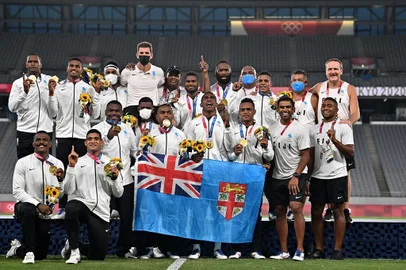 Fiji's players celebrate with their gold medals while standing on the podium after the victory ceremony following the men's final rugby sevens match during the Tokyo 2020 Olympic Games at the Tokyo Stadium in Tokyo on July 28, 2021. (Photo by Ben STANSALL / AFP) / The erroneous mention[s] appearing in the metadata of this photo by Ben STANSALL has been modified in AFP systems in the following manner: [correcting spelling of Fiji]. Please immediately remove the erroneous mention[s] from all your online services and delete it (them) from your servers. If you have been authorized by AFP to distribute it (them) to third parties, please ensure that the same actions are carried out by them. Failure to promptly comply with these instructions will entail liability on your part for any continued or post notification usage. Therefore we thank you very much for all your attention and prompt action. We are sorry for the inconvenience this notification may cause and remain at your disposal for any further information you may require.Editoria: SPOLocal: TokyoIndexador: BEN STANSALLSecao: rugby 7Fonte: AFPFotógrafo: STF<!-- NICAID(14846722) -->