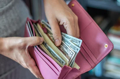 Woman taking out US dollar bills from her pocket wallet (depth of field photography)<!-- NICAID(16059127) -->