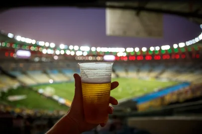 Disposable glass with beer. Soccer stadium on the backgroundConceito de cerveja em estádio - Foto: 9parusnikov/stock.adobe.comIndexador: Piotr PiatrouskiFonte: 323806559<!-- NICAID(15954049) -->