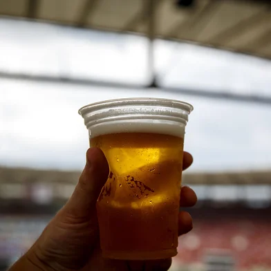 Disposable glass with beer. Soccer stadium on the backgroundConceito de cerveja em estádio - Foto: 9parusnikov/stock.adobe.comIndexador: Piotr PiatrouskiFonte: 331686098<!-- NICAID(15954048) -->