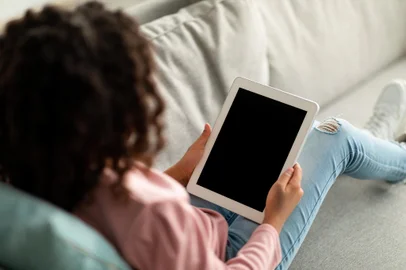 Teen african american girl holding tablet with black blank screen, using application or surfing internet at homeUso de celulares e tablets por adolescentes. Foto: Prostock-studio / stock.adobe.comFonte: 477258297<!-- NICAID(15384456) -->