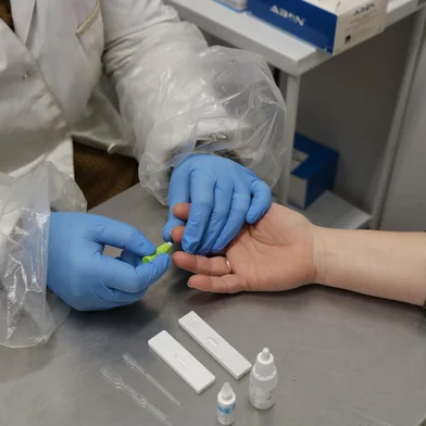 enfermeia com jaleco branco e luva azul segura a mão de uma mulher e alfineta a agulha do teste para hepatites<!-- NICAID(14845842) -->