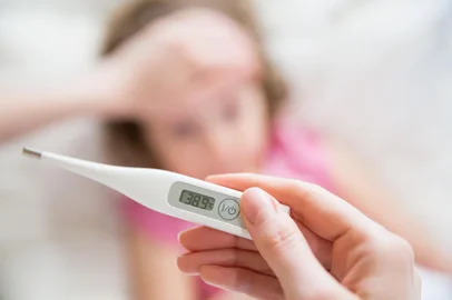 Close-up thermometer. Mother measuring temperature of her ill kid. Sick child with high fever laying in bed and mother holding thermometer. Hand on forehead.Fonte: 122235688<!-- NICAID(14985221) -->