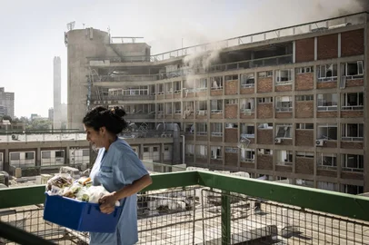 A nurse carries medical supplies past a building with smoke billowing out at Soroka Hospital following an Iranian missile attack in Beersheba in southern Israel on June 19, 2025. Soroka Hospital and two towns near Tel Aviv were struck after a barrage of Iranian missiles early on June 19, with rescuers reporting at least 47 people injured in the latest attacks. (Photo by JOHN WESSELS / AFP)<!-- NICAID(16063350) -->