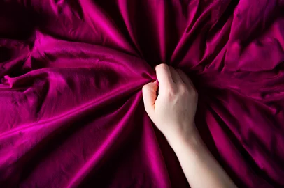 Woman hand on the silk bedding, sex and orgasm concept<!-- NICAID(15809320) -->