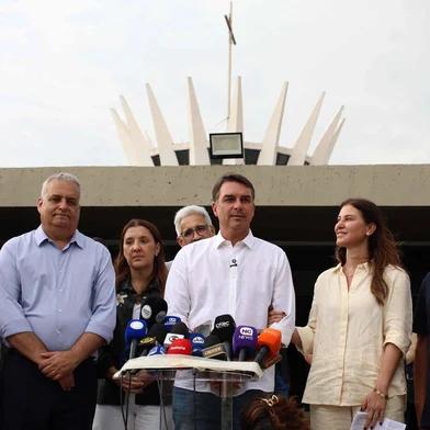 Brazil's right-wing Senator and presidential candidate for the Liberal Party (PL) Flavio Bolsonaro (C) speaks to the media alongside his wife Fernanda Bolsonaro (2-R) following a mass marking the celebration of Brazil's patron saint, Our Lady of Aparecida, at the Metropolitan Cathedral of Brasilia in Brasilia, Brazil, on October 12, 2026. (Photo by Sergio LIMA / AFP)<!-- NICAID(16385639) -->