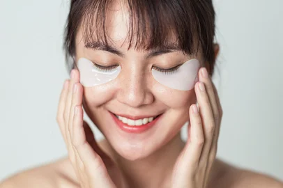 Selective focus. Asian woman smiling and applying patches mask under eyes for anti wrinkles and eye dark circles on face. Patches collagen under eyes on fresh clean skin of girl.<!-- NICAID(15989844) -->