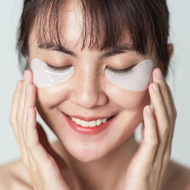 Selective focus. Asian woman smiling and applying patches mask under eyes for anti wrinkles and eye dark circles on face. Patches collagen under eyes on fresh clean skin of girl.<!-- NICAID(15989844) -->