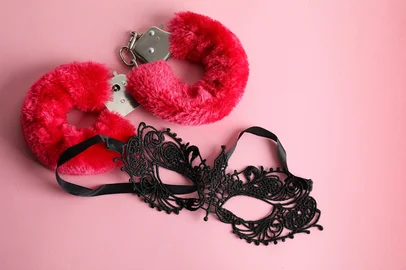 Fluffy handcuffs and lace mask on pink background, flat lay<!-- NICAID(16060853) -->