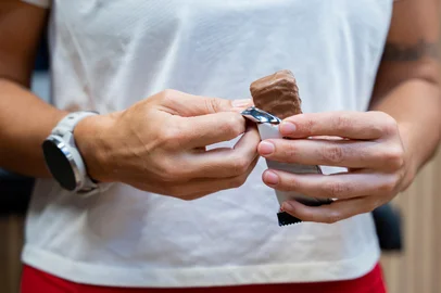 A fit woman in a gym holds a protein bar enjoying a healthy and nutritious snack to boost energy and support muscle recovery<!-- NICAID(16138871) -->