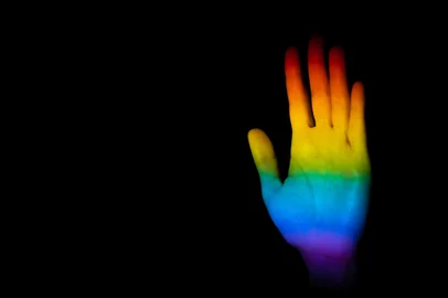 A hand making a stop gesture illuminated with the LGBT pride flag on a black backgroundA closeup of a hand making a stop gesture illuminated with the LGBT pride flag on a black background with space for text- equality conceptFonte: 435844775Fotógrafo: A hand making a stop gesture ill<!-- NICAID(15164229) -->