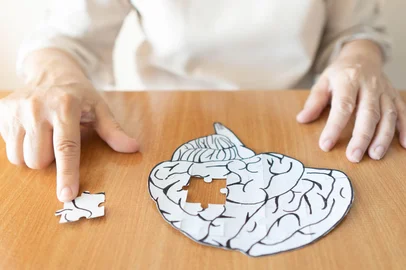 Elderly woman hands putting missing white jigsaw puzzle piece down into the place as a human brain shape. Creative idea for memory loss, dementia, Alzheimer's disease and mental health concept. Foto: Orawan / stock.adobe.comFonte: 279796511<!-- NICAID(16128498) -->