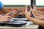 A table of high school students all holding multiple digital devices such as phones and tablets during a class lesson. Contemporary education and connected technology. No identifiable people or property visible. - Foto: LincB/stock.adobe.comFonte: 390249107<!-- NICAID(15348165) -->