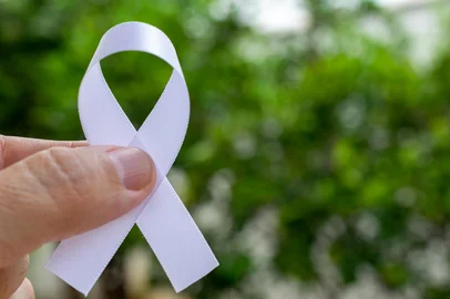 fingers holding white ribbon on green defocused background. The white ribbon represents a mental health prevention campaign. White January.Fonte: 403680389<!-- NICAID(16198469) -->