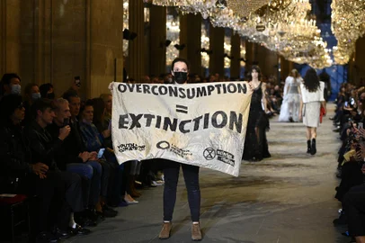A demonstrator holds a banner as models present creations by Louis Vuitton during the Women's Spring-Summer 2022 Ready-to-Wear collection fashion show as part of Paris Fashion Week at the Louvre in Paris, on October 5, 2021. - Extinction Rebellion activists burst into the Louis Vuitton fashion show at the Louvre to denounce the impact of the fashion industry on climate change, on the last day of Paris Fashion Week. (Photo by Christophe ARCHAMBAULT / AFP)<!-- NICAID(14907541) -->