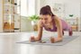 Sporty young woman doing plank exercise on yoga mat and using fitness app on cellphoneBeautiful fit young woman having sports workout at home, doing plank exercise on yoga mat, trying to endure physical exertion and using modern fitness mobile app on her cellular phoneFonte: 617487398<!-- NICAID(15497530) -->
