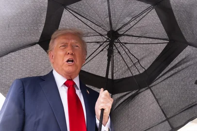 US President Donald Trump holds an umbrella as he speaks to reporters before boarding Air Force One prior to departure from Joint Base Andrews in Maryland, October 12, 2025. Trump is travelling to Israel, where he will address parliament and meet with hostage families, before heading to Egypt's Sharm El-Sheikh for a major peace summit, where a "document ending the war in the Gaza Strip" is expected to be signed, according to Cairo's foreign ministry. (Photo by SAUL LOEB / AFP)<!-- NICAID(16144514) -->