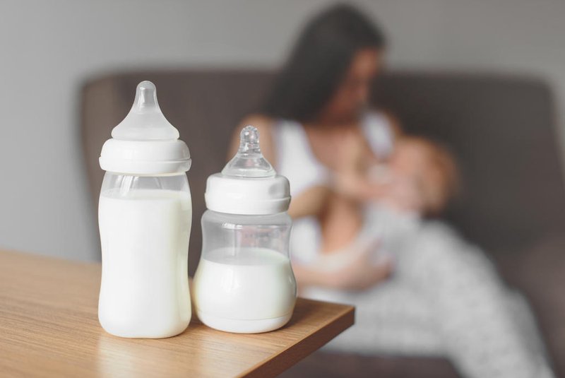 Bottles with breast milk on the background of mother holding in her hands and breastfeeding baby. Maternity and baby care.Amamentação, leite materno - Foto: evso/stock.adobe.comIndexador: Evgeniia SobolevskaiaFonte: 193809344<!-- NICAID(15763723) -->