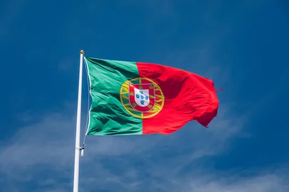 Beautiful large Portuguese flag waving in the wind against blue sky. Portuguese Flag Waving Against Blue Sky. Flag of Portugal waving, against blue sky <!-- NICAID(16051232) -->