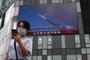 A woman uses her mobile phone as she walks in front of a large screen showing a news broadcast about China's military exercises encircling Taiwan, in Beijing on August 4, 2022. - China's largest-ever military exercises encircling Taiwan kicked off August 4, in a show of force straddling vital international shipping lanes after a visit to the island by US House Speaker Nancy Pelosi. (Photo by Noel Celis / AFP)<!-- NICAID(15167028) -->