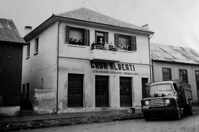 Casarão da família Guerra em meados de 1955, quando funcionava no térreo o Armazém Alberti, um secos e molhados administrado pela família de Armando Alberti. O local é a  Rua Pinheiro Machado, entre as ruas Marechal Floriano e Moreira César, onde hoje funciona o Café com Mistura, administrado por Sérgio Guerra. Na varanda estão Jerônimo Guerra e Judite Mezzomo Guerra com os netos Oscar, Reni e Clélia. Na janela da direita estão o casal Antônio (filho de Jerônimo) e Angelina Guerra com o fillho Pedro. Na janela da esquerda aparecem Maria e Leonilda, irmãs de Antônio. O caminhão estacionado pertenceu a Antônio Guerra e era utilizado para fretes entre Caxias do Sul e Porto Alegre. Obs.: Sérgio Guerra, filho de Antônio e atual administrador do café, ainda não havia nascido.<!-- NICAID(16232276) -->