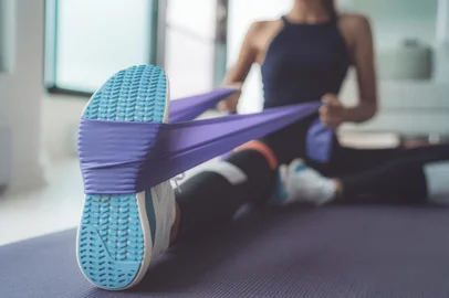 Resistance band exercise at home. Woman doing pilates workout using elastic strap pulling with arms for shoulder training on yoga mat indoors.<!-- NICAID(15682012) -->