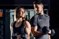 A happy sporty couple doing exercises for biceps with barbells in a gym and making eye contact with each other.Indexador: dusan petkovicFonte: 484487703<!-- NICAID(15577992) -->