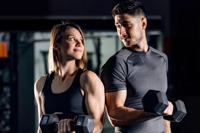 A happy sporty couple doing exercises for biceps with barbells in a gym and making eye contact with each other.Indexador: dusan petkovicFonte: 484487703<!-- NICAID(15577992) -->